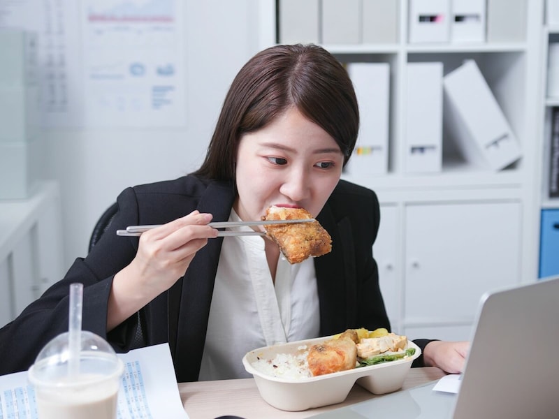 忙しい仕事の合間に揚げ物を食べる社会人女性の食事シーン