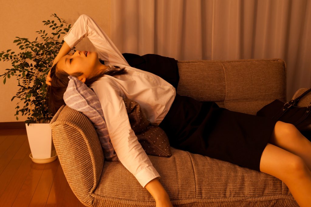仕事の疲れからソファで眠ってしまう社会人女性の様子