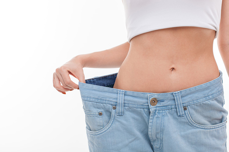 ウエスト部分にゆとりができたデニムを引っ張る女性。体重が変わらなくても見た目が変わることを表現した写真。